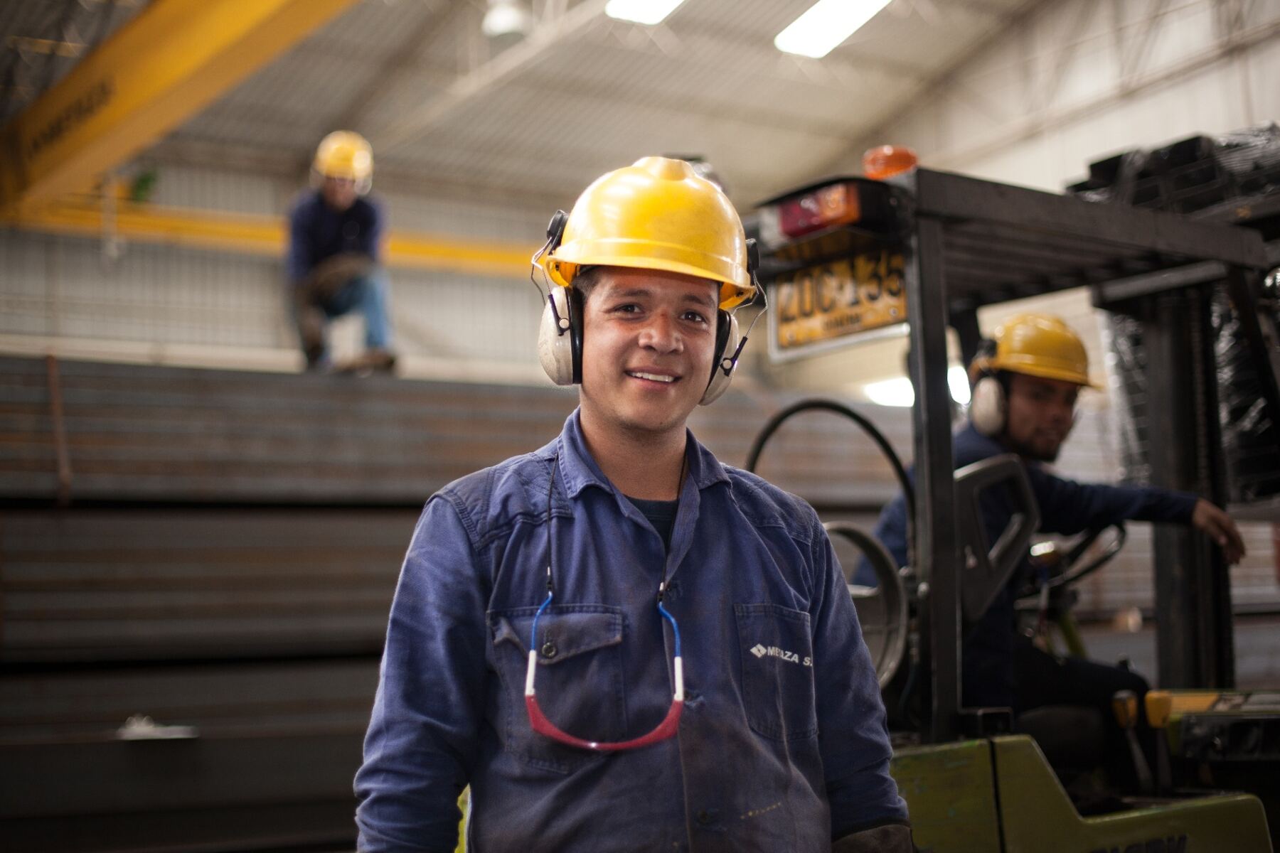 Operario industrial sonriente con casco y montacargas